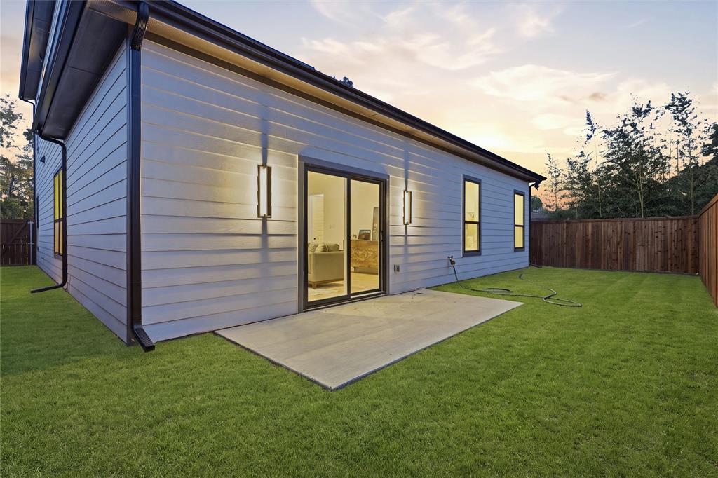 Horizontal lap siding exterior featuring a concrete patio, sliding glass door, linear wall-mounted outdoor lighting, and wood-panel perimeter fencing