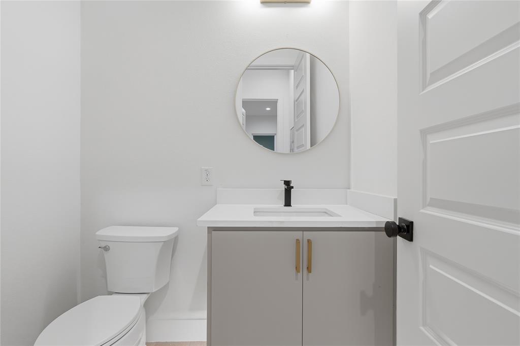 Vanity featuring a light gray cabinet with metal pulls, white countertop, integrated rectangular sink, matte black faucet, and circular wall-mounted mirror