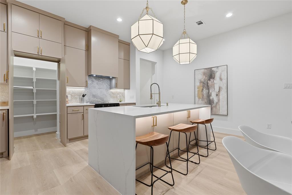 Kitchen featuring a central island with a waterfall-edge countertop, floor-to-ceiling cabinetry, geometric pendant lighting, walk-in pantry, and wood-finish flooring Kitchen featuring a central island with a waterfall-edge countertop, floor-to-ceiling cabinetry, geometric pendant lighting, walk-in pantry, and wood-finish flooring