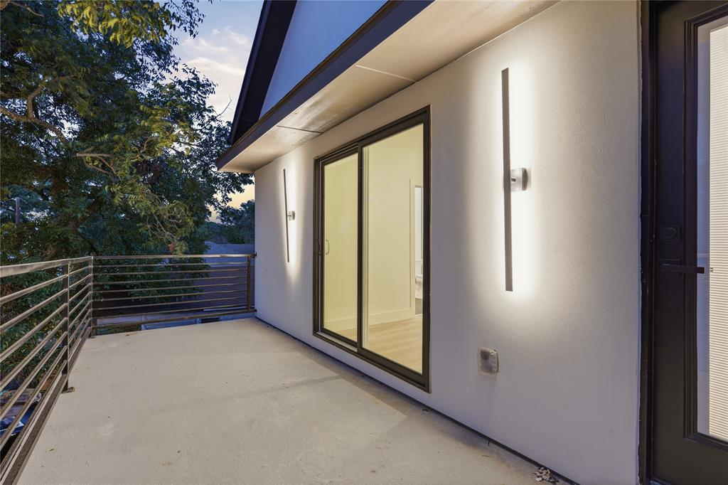 Covered balcony featuring horizontal metal railings, sliding glass door, and linear wall-mounted lighting