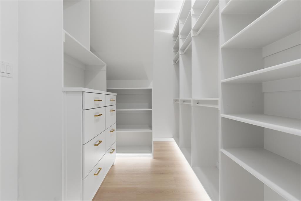 Custom storage organization featuring white built-in cabinetry, floor-to-ceiling shelving, integrated hanging rods, drawers with metallic pulls, and wood-finish flooring