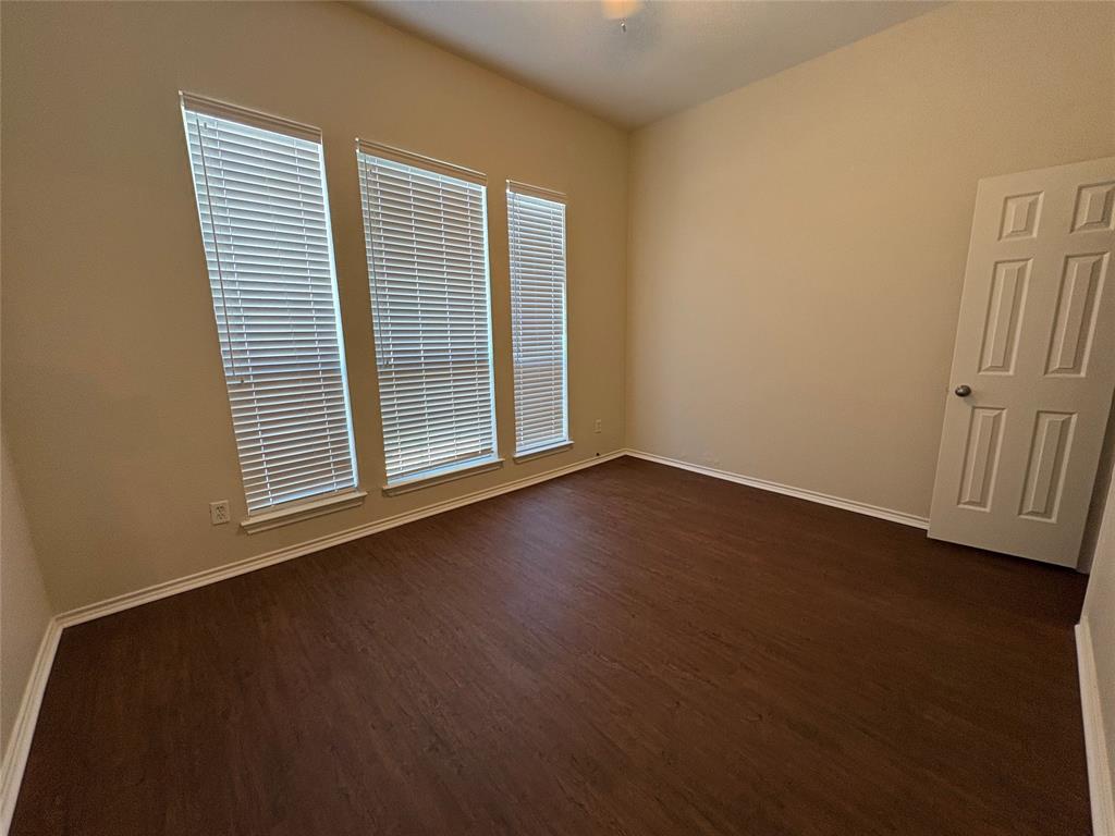High-ceiling room featuring dark wood-finish flooring, three vertical windows with installed blinds, and a paneled interior door