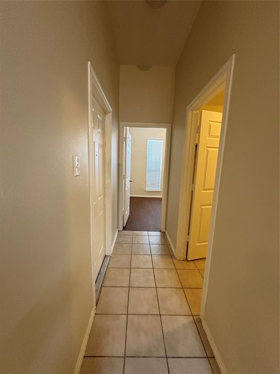 Hallway featuring ceramic tile flooring, neutral wall tones, multi-panel interior doors, and a window with horizontal blinds