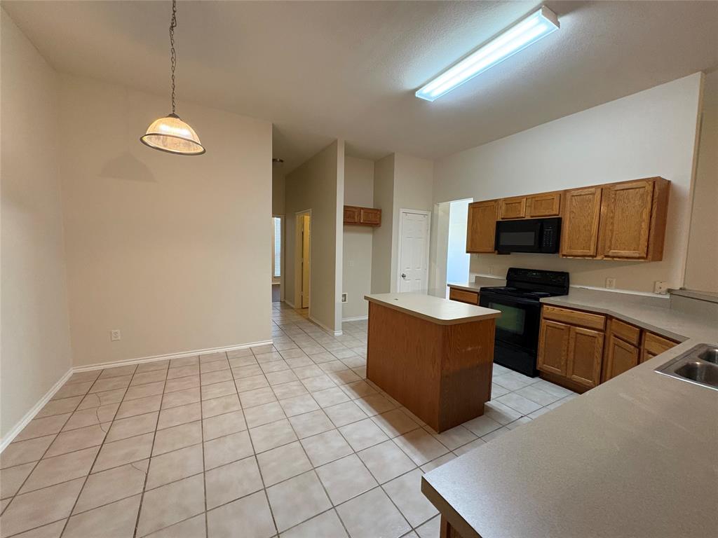 Kitchen featuring wood cabinetry, a center island with solid-surface countertop, tile flooring, and integrated black appliances