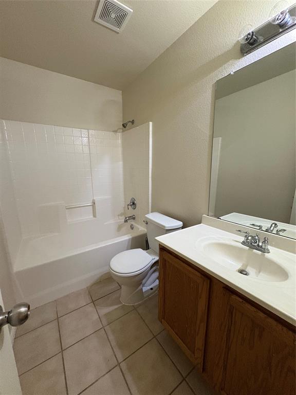 Bathroom featuring a combination tub and shower with tile surround, wood-finish vanity cabinet with a white countertop, oval drop-in sink, and full-width vanity mirror