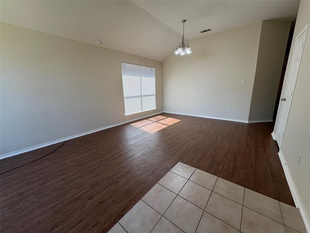 Vaulted ceiling with an integrated multi-light chandelier, wood-finish flooring, neutral wall paint, and ceramic tile flooring entry