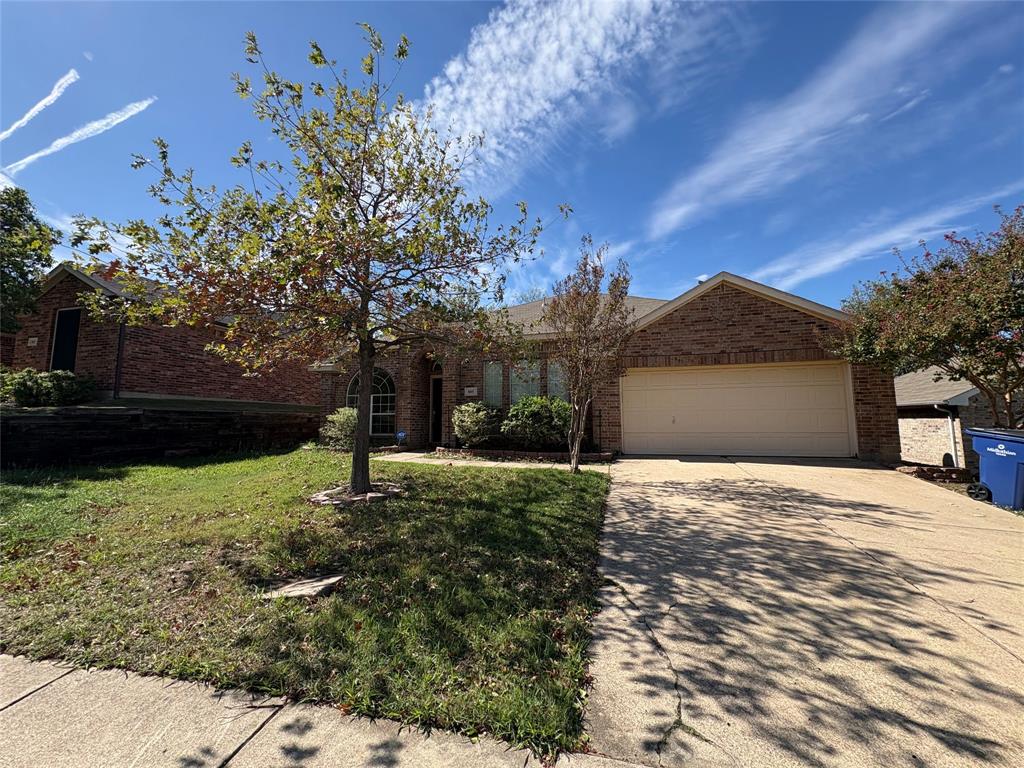 Single-story brick exterior featuring a multi-gabled roofline, front-facing two-car garage, concrete driveway, and mature landscaping