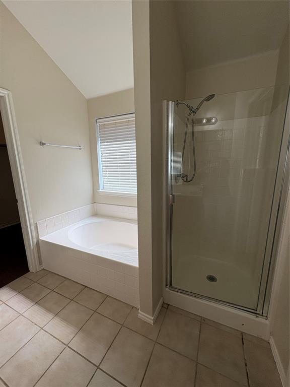 Bathroom featuring a tiled floor, soaking tub with white tile surround, and a glass-enclosed shower with a handheld showerhead