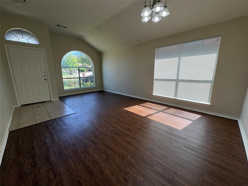 Open-concept space featuring vaulted ceilings, wood-finish flooring, a neutral color palette, arched window detailing, and an entry area with tile flooring