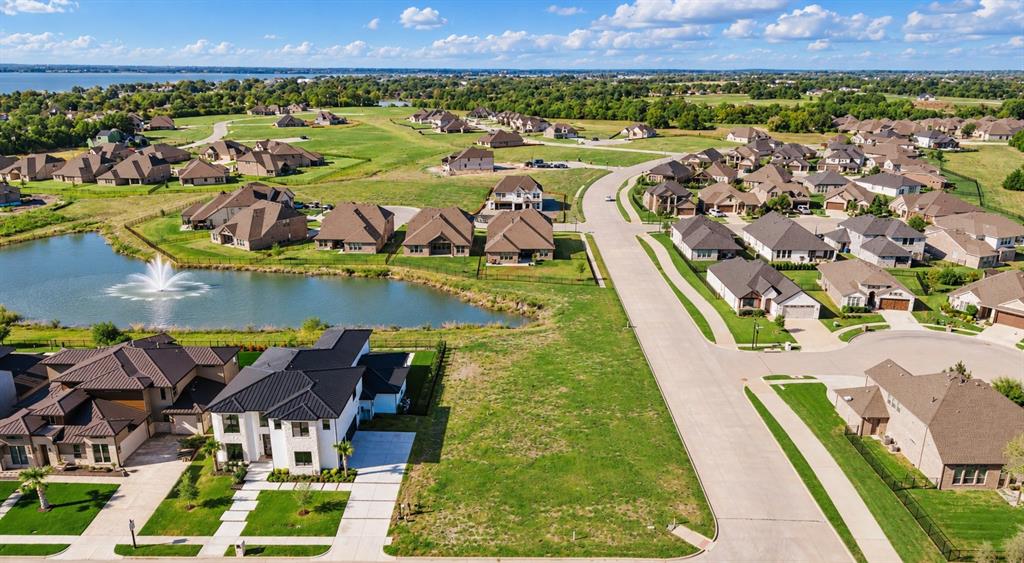 Aerial perspective showcasing a residential community with paved streets, landscaped grounds, a central pond featuring a fountain, and proximity to a large body of water