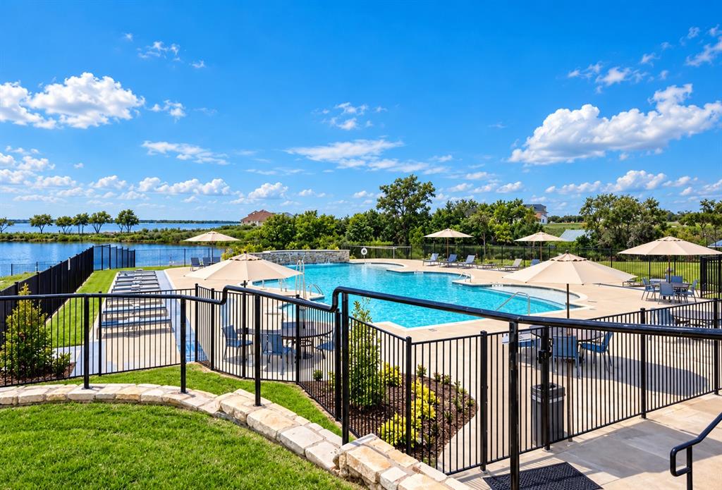 Community swimming pool with stone-accented water feature, concrete deck, and metal perimeter fencing overlooking a lake