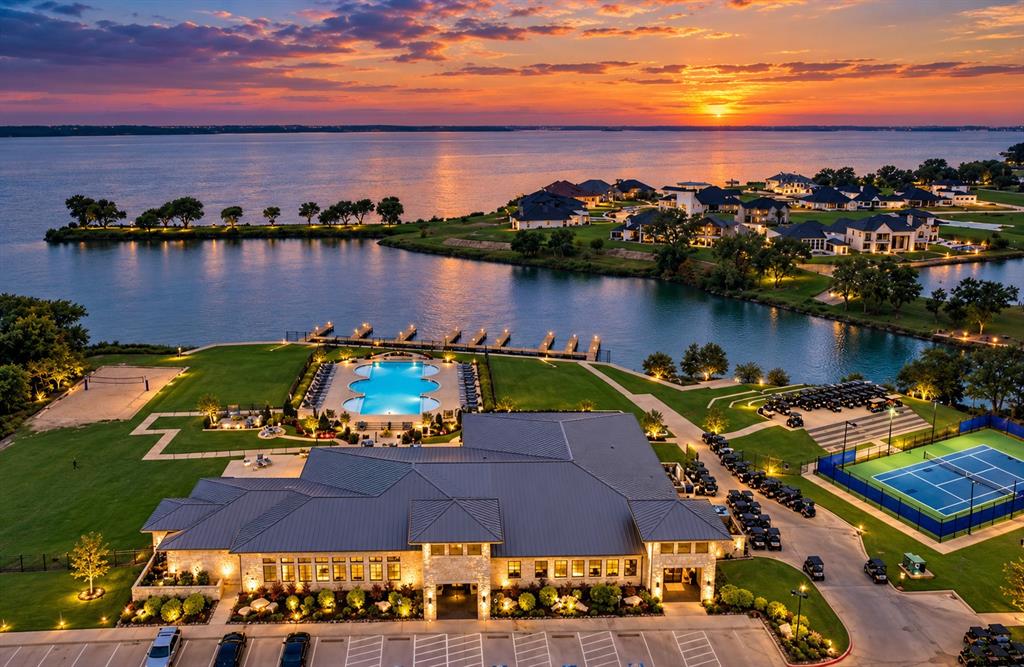 Aerial perspective of property amenities featuring a multi-section swimming pool, hard-surfaced tennis court, private boat docks, and expansive waterfront lawn