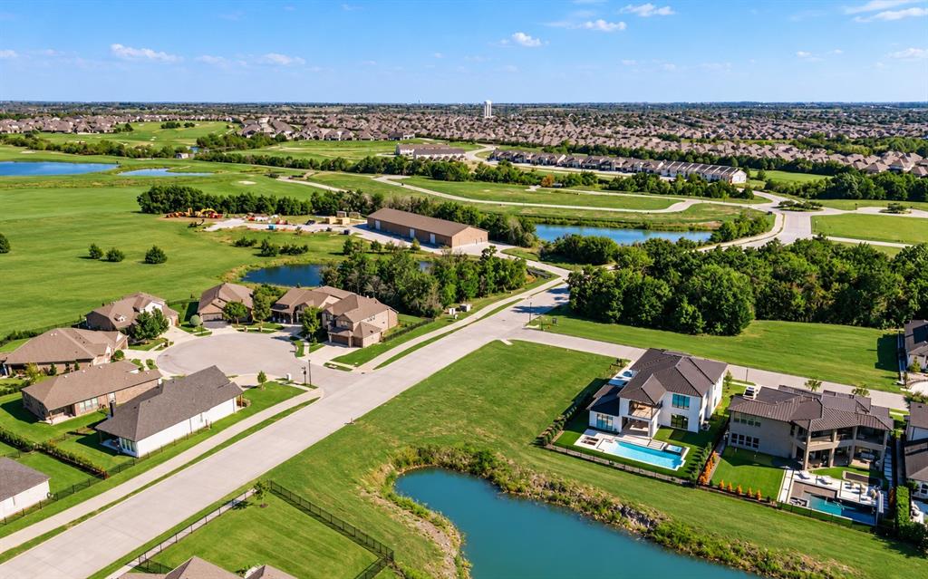 Aerial perspective of a residential neighborhood featuring expansive green space, manicured lawns, paved streets, and multiple water features