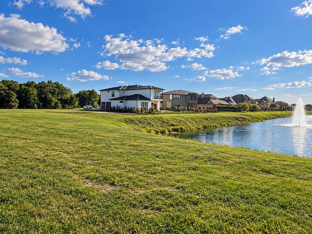 Expansive waterfront property featuring a manicured lawn, an active water fountain, and mature tree lines