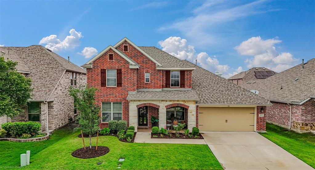 Traditional home featuring brick siding, a shingled roof, an attached garage, concrete driveway, and a front lawn