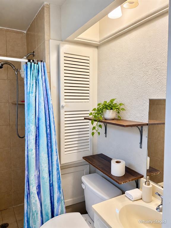 Full-height beige tile shower surround with integrated shelving, built-in floor-to-ceiling louvered storage cabinetry, and dual floating wood shelves