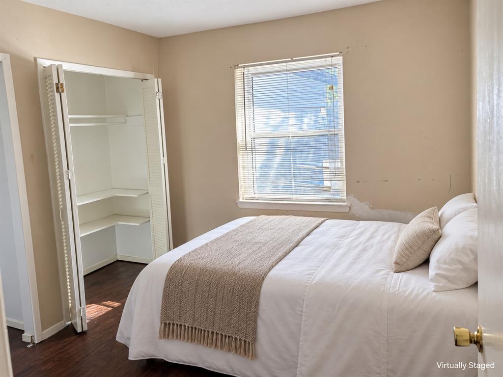 Room featuring dark wood-finish flooring, a double-hung window with built-in blinds, and a closet with bifold louvered doors and interior shelving
