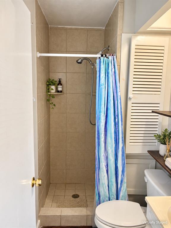 Walk-in shower enclosure featuring floor-to-ceiling neutral tile, a built-in corner shelf, and a wall-mounted showerhead, complemented by louvered cabinetry and built-in wood shelving