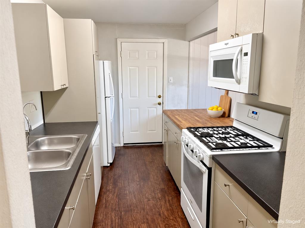 Kitchen featuring wood-finish flooring, solid-surface countertops, wood-block prep station, white cabinetry, and stainless-steel dual-basin sink