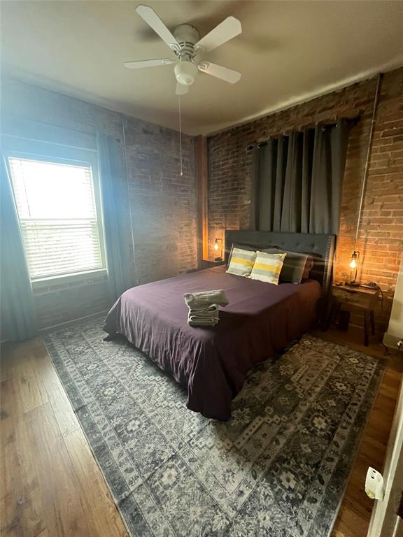 Exposed brick wall finishes, wood-finish flooring, and a white ceiling fan with integrated lighting