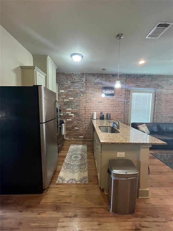 Kitchen featuring an exposed brick wall, stone-surface breakfast bar with an integrated stainless steel sink, wood-finish flooring, and pendant lighting