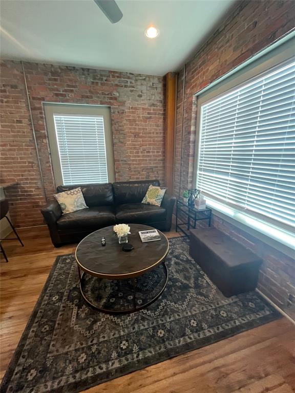 Exposed brick walls, wood-finish flooring, and large windows with horizontal blinds