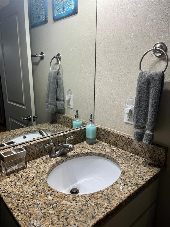 Vanity featuring a stone-composite countertop with an integrated oval under-mount sink, brushed-nickel widespread faucet, large-format mirror, and circular wall-mounted towel ring