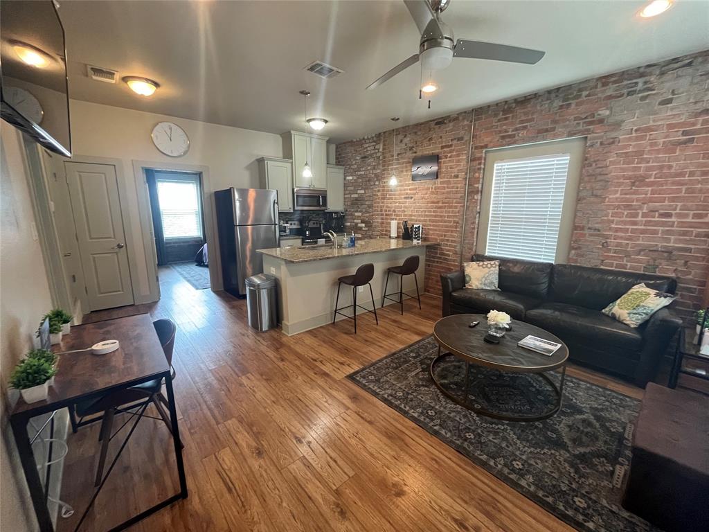 Exposed brick wall, wood-finish flooring, kitchen island with stone countertop, stainless steel refrigerator, and ceiling fan