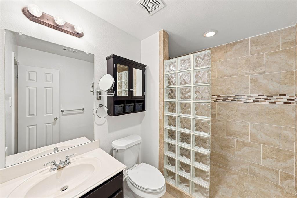 Bathroom featuring a shower stall with a glass block partition, decorative tile accent wall, vanity with an integrated sink, and wall-mounted light fixture