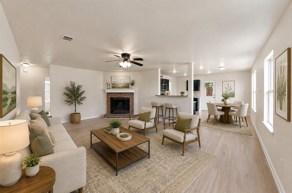 Open-concept living space featuring wood-finish flooring, a brick fireplace with a mantle, recessed lighting, and a kitchen pass-through counter