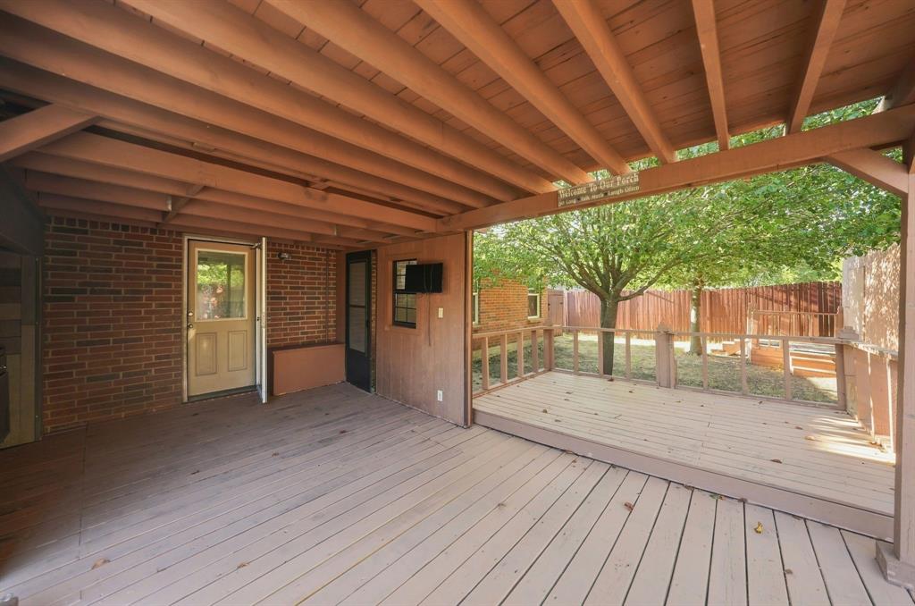 Covered wood deck featuring an exposed beam ceiling, brick exterior wall, and wooden perimeter railing