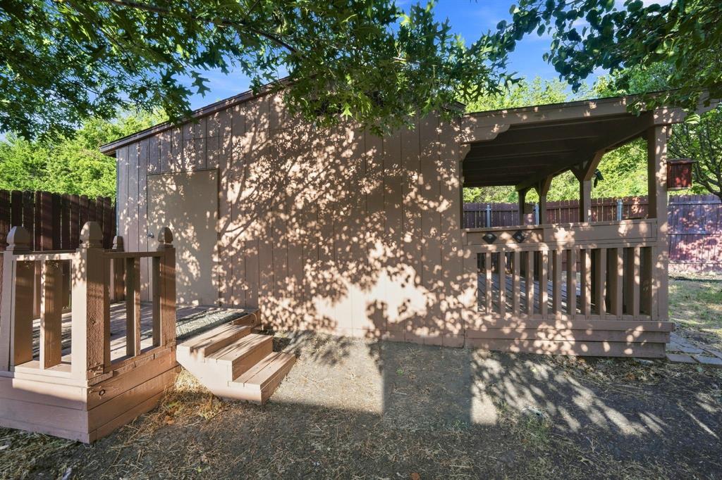 Outdoor structure featuring a covered porch, a side deck with stairs, vertical wood-finish siding, and a wood railing system