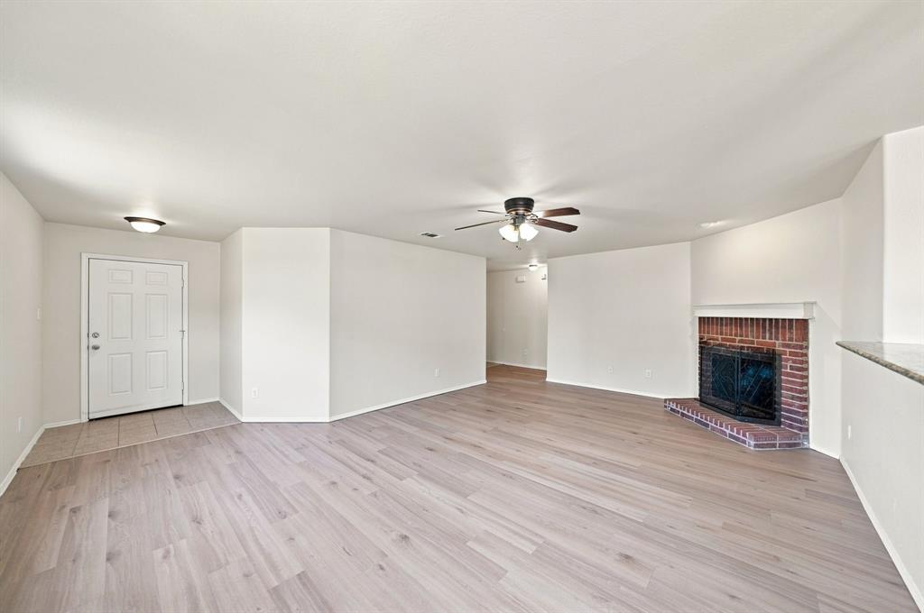 Living area featuring wood-finish flooring, a brick fireplace with a mantel, a ceiling fan with light fixture, and tile entryway flooring
