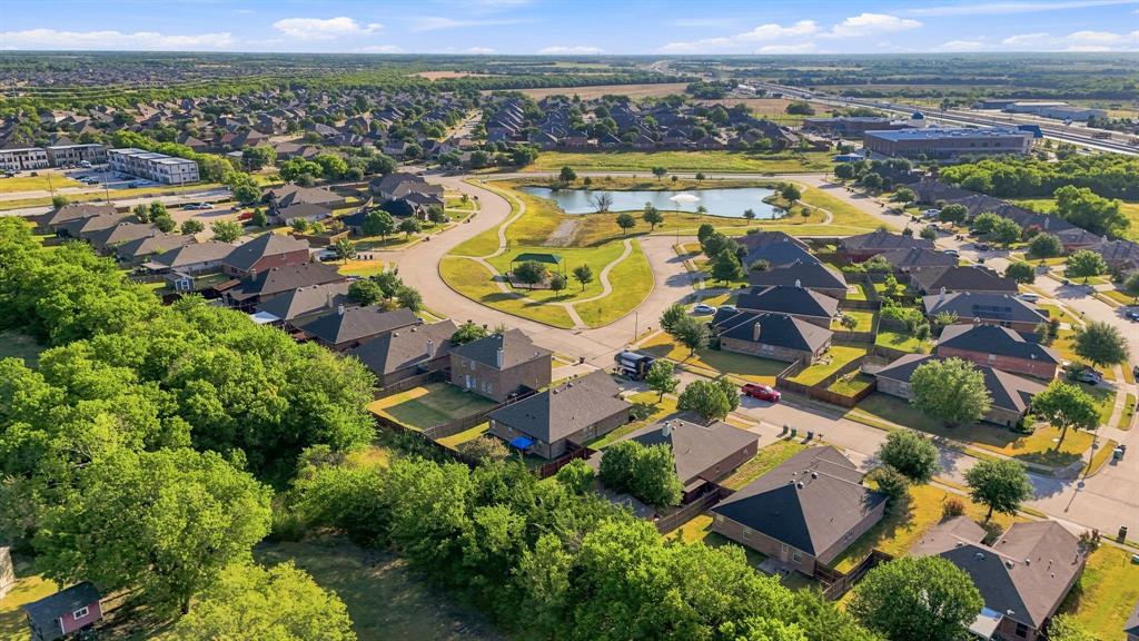 Aerial perspective featuring a community pond, manicured green space, pedestrian paths, and mature trees