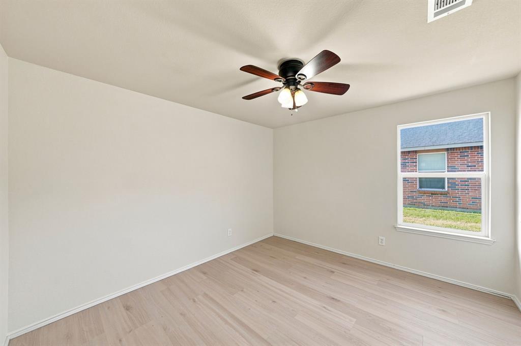 Neutral-toned interior space featuring wood-finish flooring, a ceiling fan with integrated lighting, and a single window