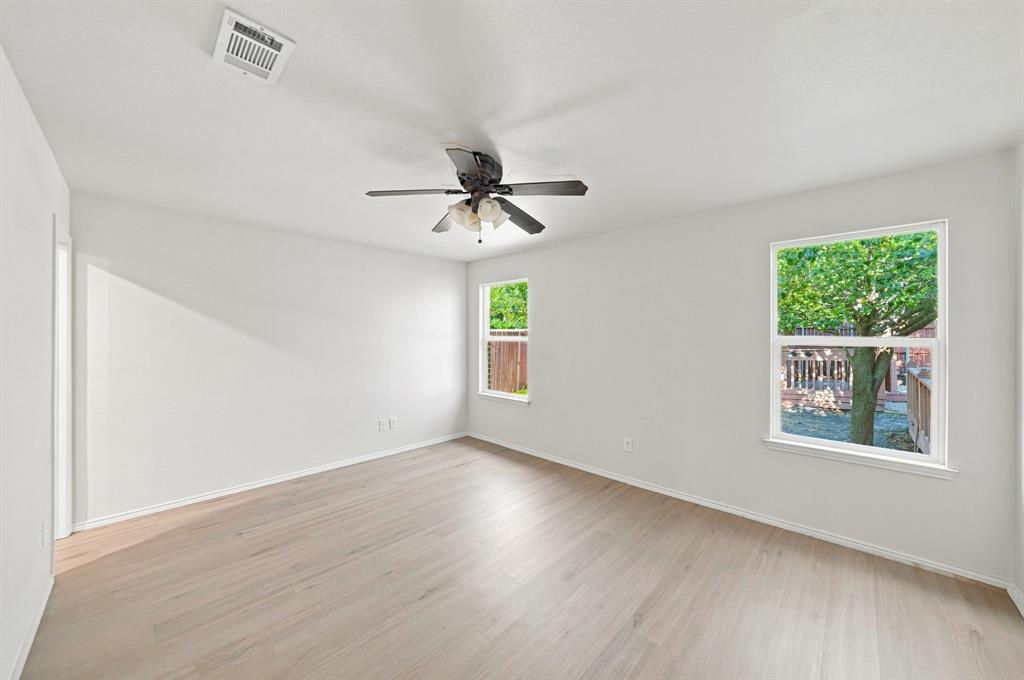 Room featuring light-toned wood-finish flooring, neutral walls, two windows, and a ceiling fan with integrated lighting