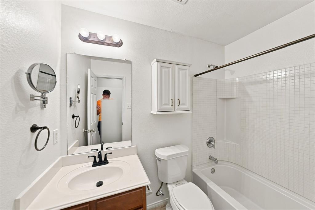 Bathroom featuring a vanity with integrated sink, wall-mounted cabinet storage, three-light fixture, and a tub-shower combination with square tile surround