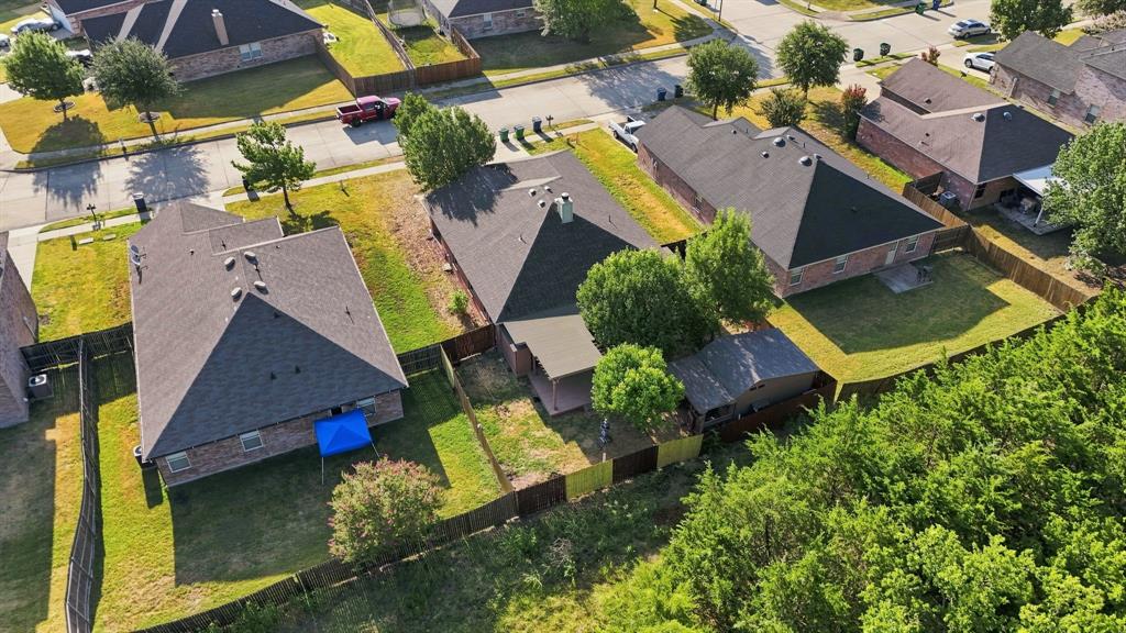 Aerial perspective of a brick exterior home featuring a composition shingle roof, a rear covered patio, a fenced backyard, and established trees