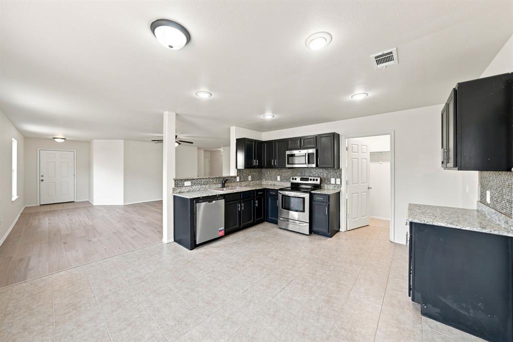 Kitchen featuring dark-finish cabinetry, stone-style countertops, stainless steel appliances, tile flooring, and flush-mount lighting