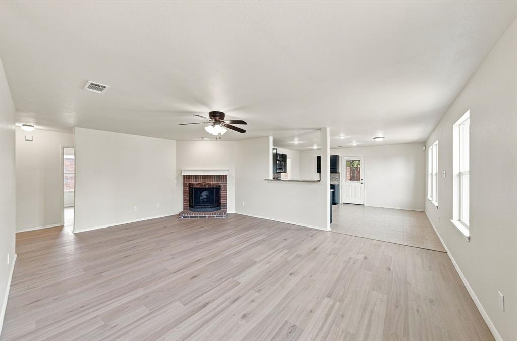 Open-concept living space featuring wood-finish flooring, a brick fireplace with a mantel, a ceiling fan, and tile flooring in the kitchen area