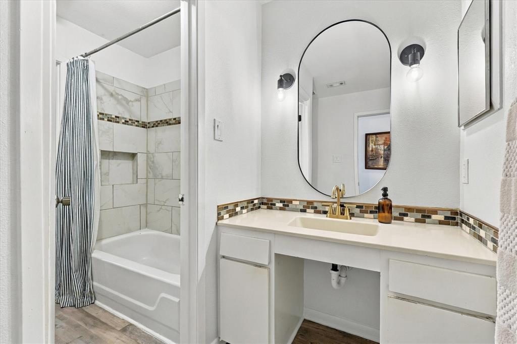 Bathroom featuring a vanity with a solid-surface countertop, an integrated sink, polished metal hardware, an oval wall mirror, and a tiled shower surround with a decorative glass mosaic inlay
