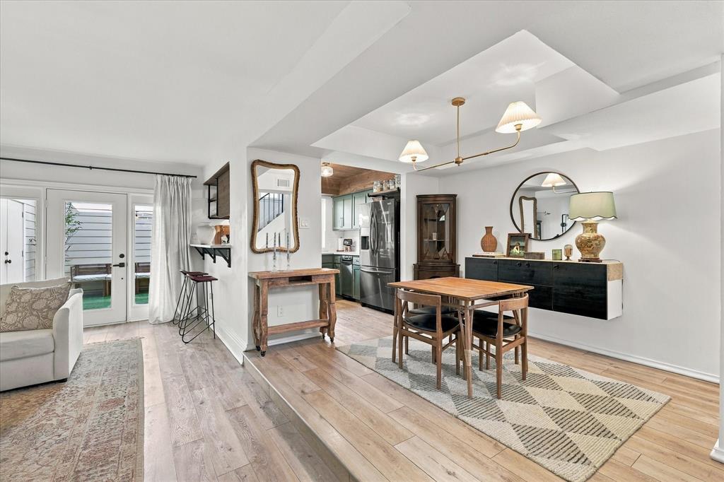 Dining area featuring a tray ceiling with a multi-light chandelier, wood-finish flooring, and a glass-paned door providing external access