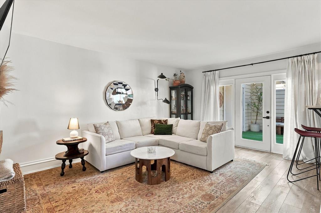 Living area featuring wood-finish flooring, dual-arm wall-mounted lighting, and glass-paneled exterior doors with access to an outdoor space