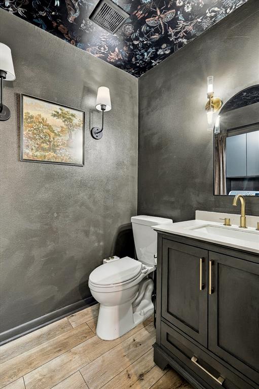 Bathroom featuring a dark vanity with a light-colored countertop, brass-finish faucet and hardware, wood-finish flooring, and a patterned ceiling treatment with dual wall-mounted light fixtures