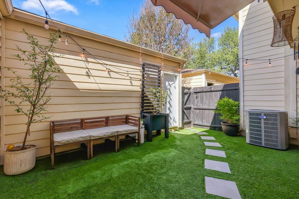 Outdoor courtyard featuring synthetic turf, square stone paver pathway, retractable wall-mounted awning, vertical wood privacy screening, and horizontal lap siding