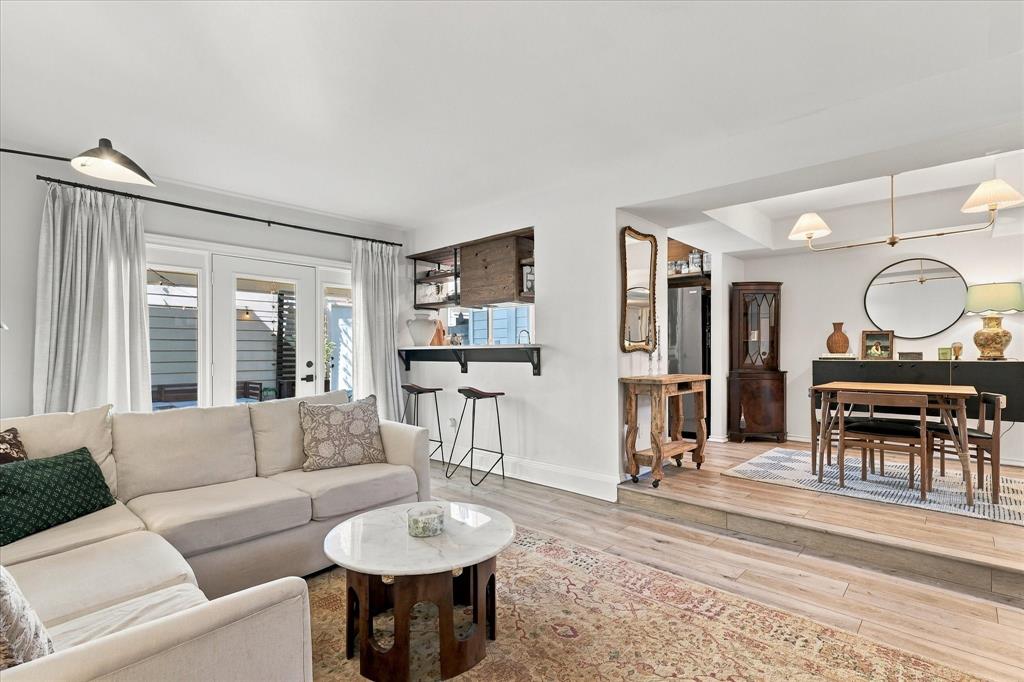 Living area featuring wood-finish flooring, a pass-through bar with built-in cabinetry, dual glass-paned doors, and a multi-level floor plan with a raised dining area