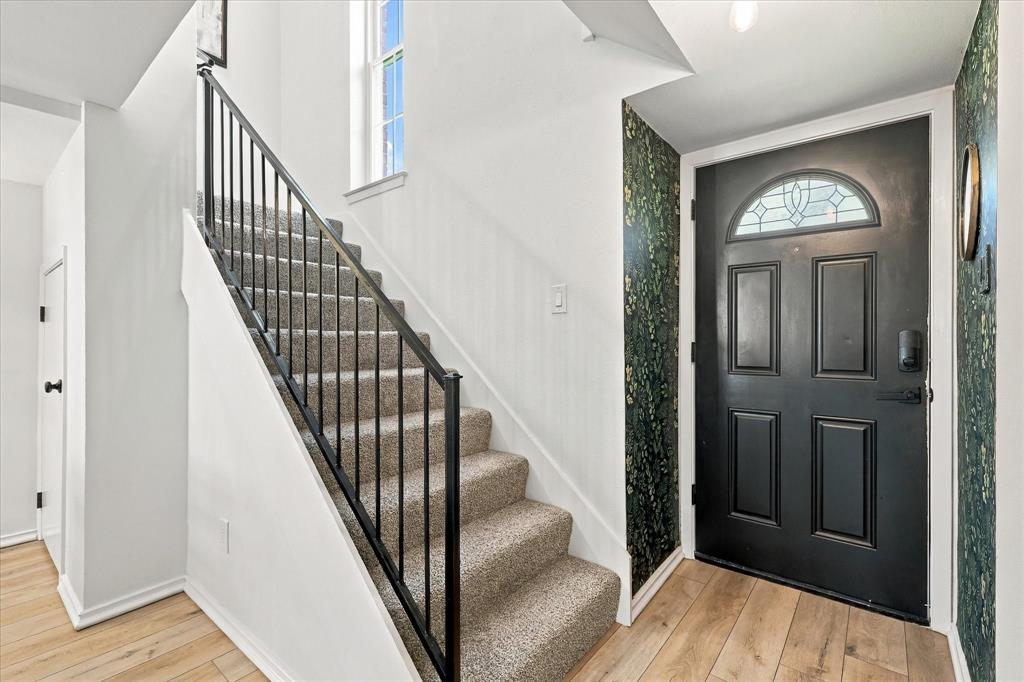 Entryway featuring a black four-panel door with arched transom window, metal handrail, staircase with carpeted treads, and wood-finish flooring