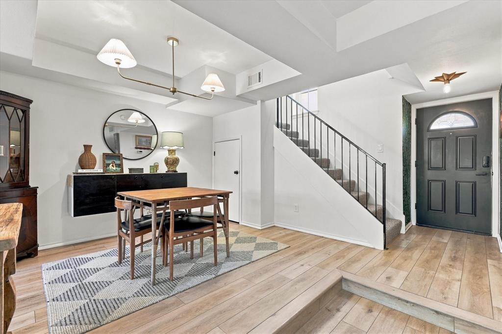Entry featuring wood-finish flooring, recessed tray ceiling, multi-arm metallic light fixture, and a staircase with a black metal railing