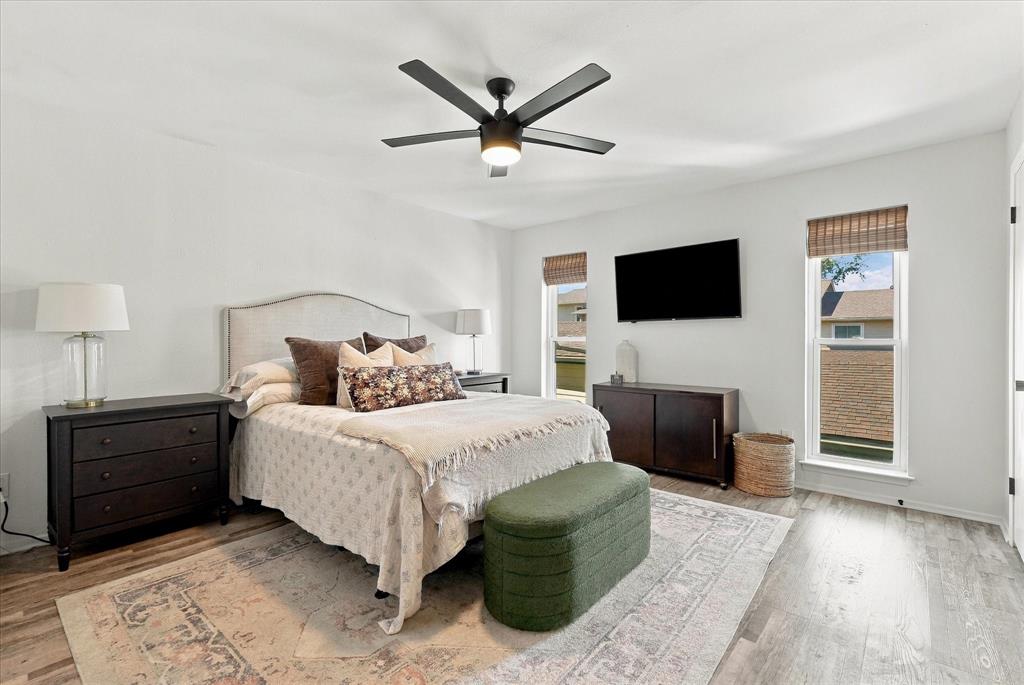 Room featuring wood-finish flooring, a matte black multi-blade ceiling fan with integrated lighting, and two windows with installed window shades