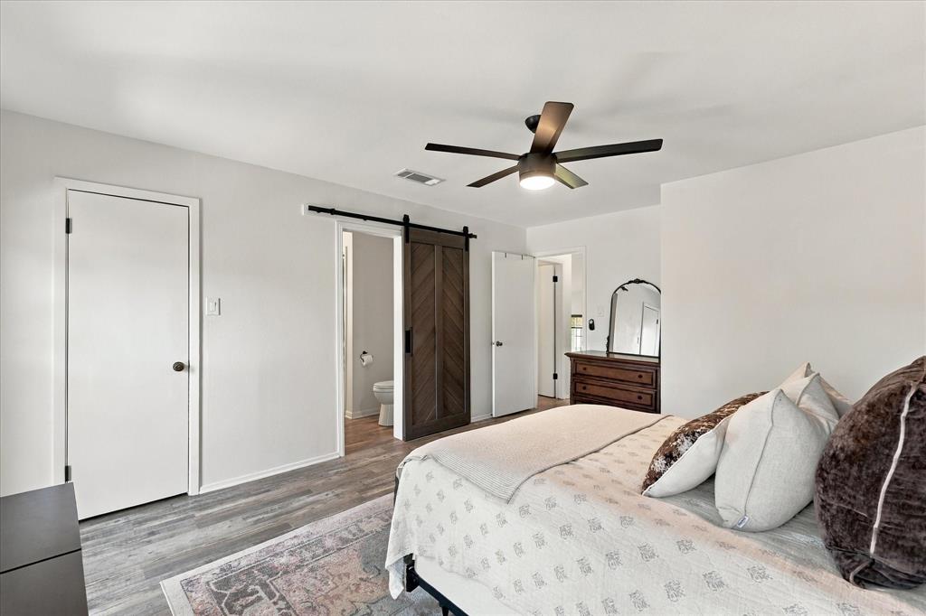 Room featuring wood-finish flooring, a herringbone-pattern sliding barn door, and a multi-blade ceiling fan with integrated lighting
